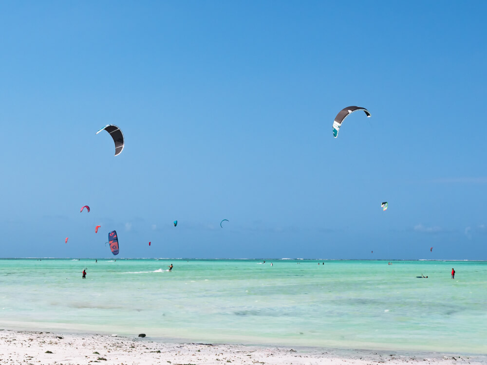 Kitesurfers with colorful kites surfing in the shallow clear waters of Paje, one of the best activities in Zanzibar for watersports enthusiasts.