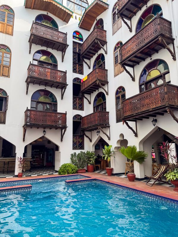 A courtyard with a pool and balconies with wooden carvings and stained glass windows in Dhow Palace Hotel.