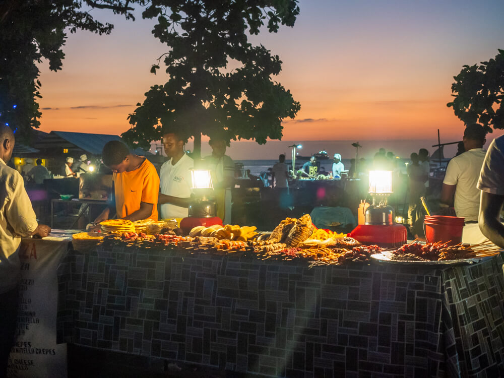 Local men preparing food, with various skewers of meat and seafood displayed in front of them at Forodhani street food market.