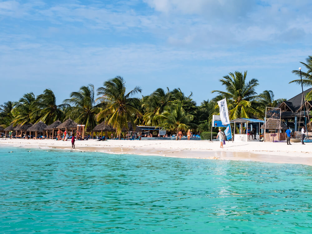 Turquoise sea and a busy white sand beach lined with palm trees and parasols in Kendwa, Zanzibar.