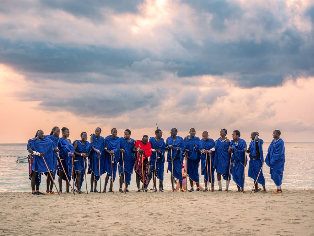 A group of Maasai men with blue robes standing in a row as they perform on Kendwa Beach.