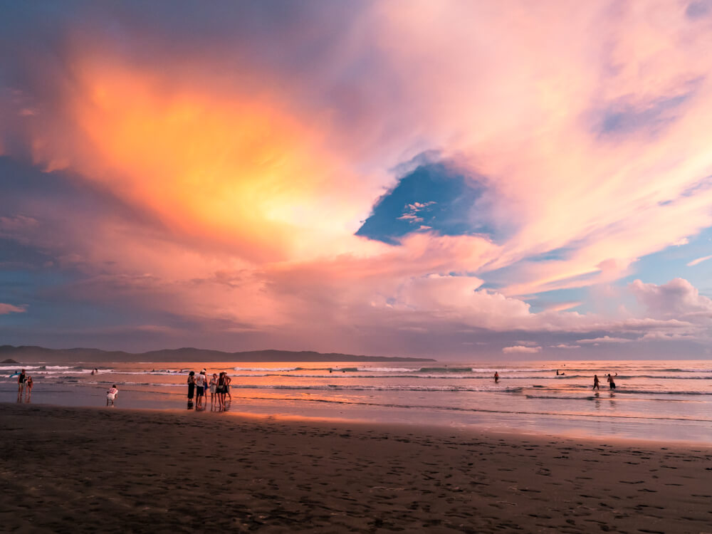 A sky full of orange and pink clouds and a black sand beach during sunset in Santa Catalina, Panama