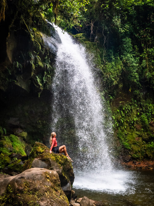 Me sitting on a rock in front of a waterfall surrounded by lush green vegetation in Boquete, Panama.