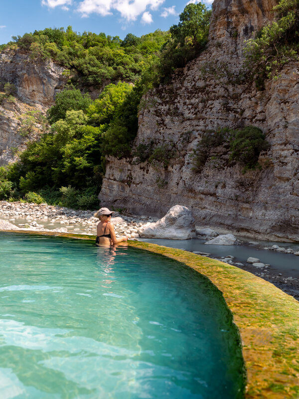 Me relaxing in a turquoise pool at Benja Thermal Baths in Albania, with the steep limestone walls of Langarica Canyon in the background.