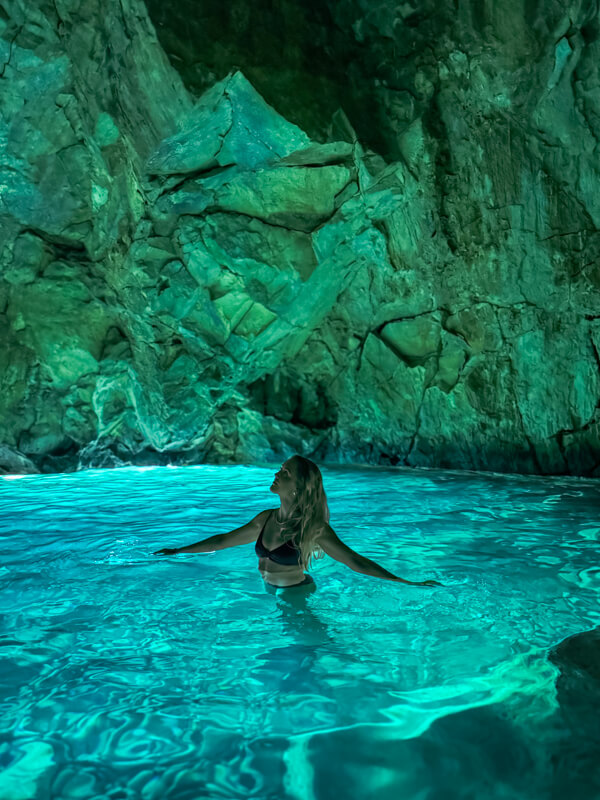 Me wading in the luminous turquoise water inside the Blue Cave with jagged rock walls above me, one of the highlights of this Albania itinerary.