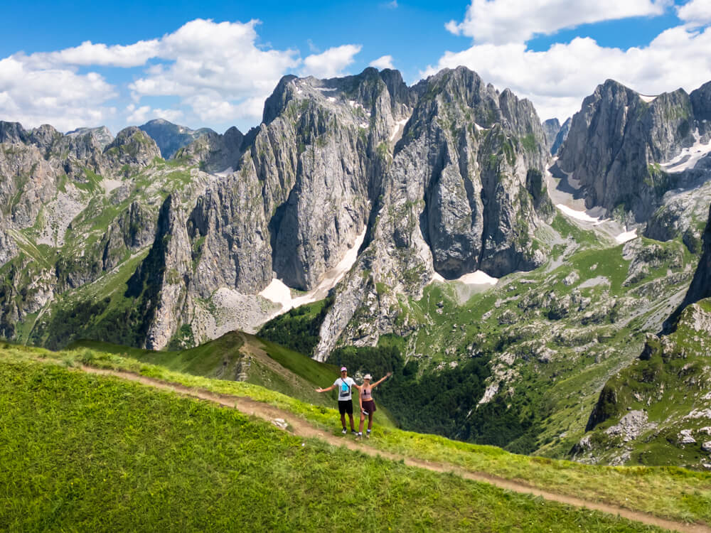 My husband and I posing in front of jagged grey limestone peaks on the Maja e Vajushes trail, one of the most scenic hikes in Albania.