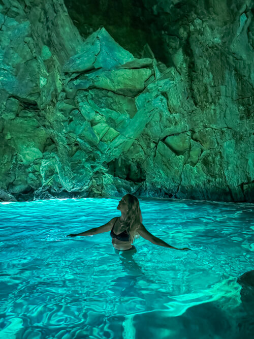 Me wading in the vivid turquoise water inside the Blue Cave on the Albanian Riviera with jagged rock walls around me.